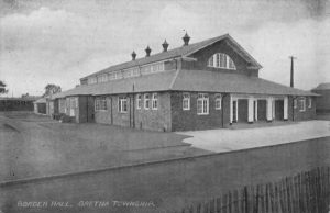 A large, wide, hall building with two rows of windows. In front of the building is a road. A driveway encircles the building. Text on the photo reads 'Border Hall, Gretna Township.' This photo is in black and white.