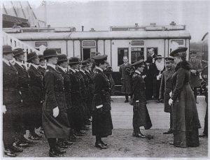 The woman's police force lined up at a train station. King George V and Queen Mary stand before them. This is a black and white archive photo.