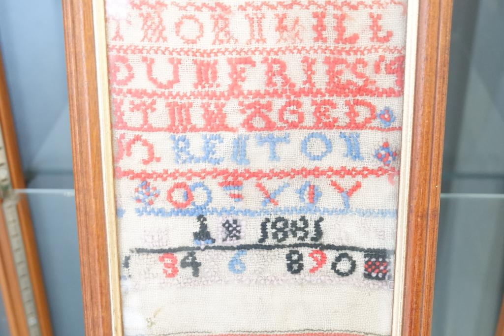 Some embroidered letters in a display case.