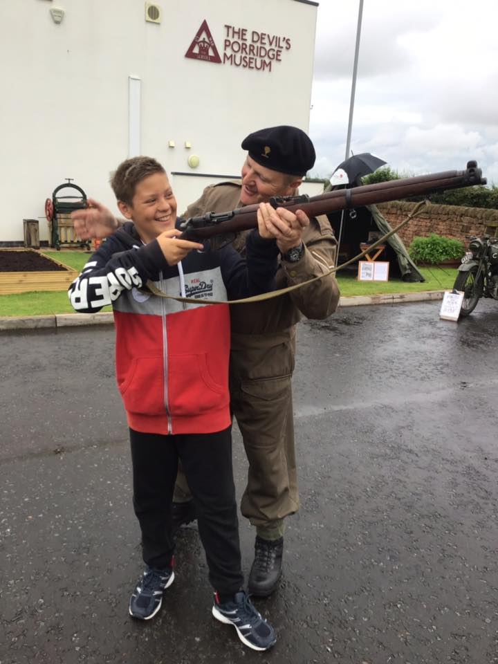 A living history reenactor stands beside a child holding a replica gun. They look happy.