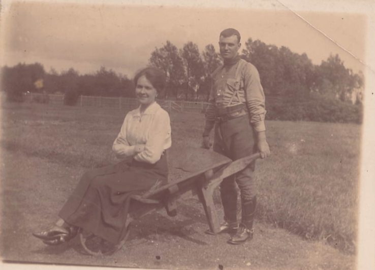 A lady sitting in a wheelbarrow with a man pushing it. This is an archive photo.