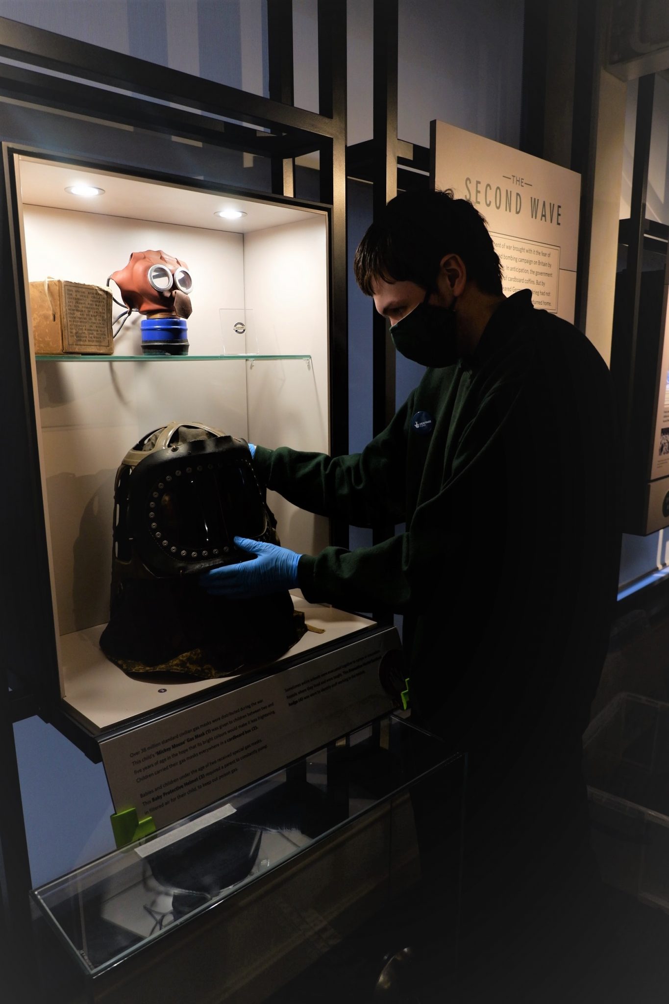 A person lifting a gas mask from a display case.