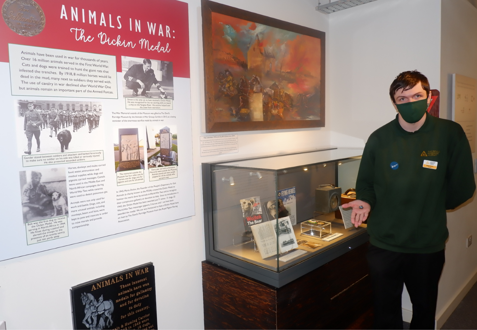 A young person holding a badge in front of The Animals in War display.