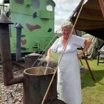 A smiling living history reenactor cooking some food.