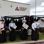 Four happy living history reenactors dressed as suffragettes with placards outside The Devil's Porridge Museum.