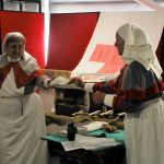 Two reenactors dressed as nurses handing something to each other.