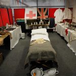 The Devil's Porridge Museum's education room filled with tables containing items from the past with a bed in the middle.