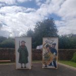 Some people putting their faces through signs so they look like a soldier and a suffragette.