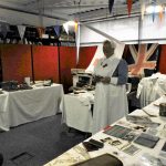 A room with tables full of equipment and photos from the past and two people dressed as WW1 nurses.