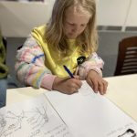 A child drawing and writing on a clipboard.