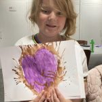 A child proudly holding their finished ink art. They look happy.
