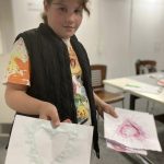 A young person holding their finished ink art. Two bits the art depict heart shapes.