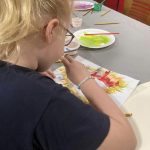 Another child creating ink art with a straw on a piece of paper.
