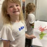 A smiling child holding some ink artwork they created.
