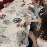 A table filled with beads and jewellery materials with young people sat around it.