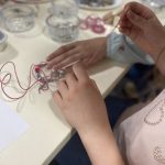 A young person holding a string used to make jewellery.