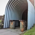 A metal Anderson shelter with two wooden benches inside.