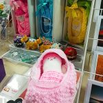 A knitted baby made by the Scotia Crafters. In the background are some more knitted babies and some pin cushions.