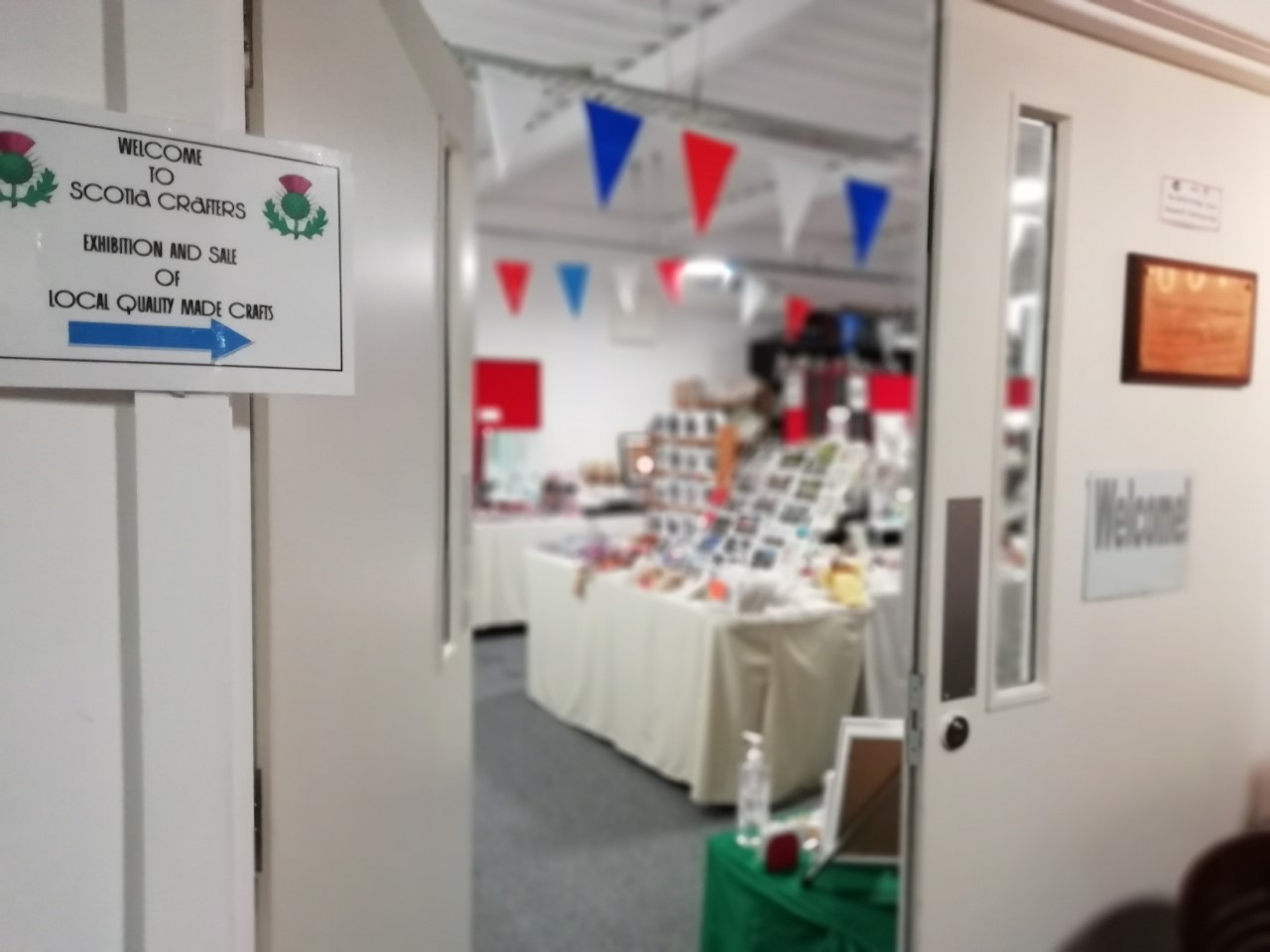 A sign for the Scotia Crafters pointing through the open door of The Devil's Porridge Museum's education room in which tables of local crafts are displayed.