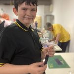 One of the young members of Annan Bee Club holding a handmade wax candle and looking happy.