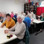 Three rows of tables with members of The Devil's Porridge Museum's Cordite Club sat at them. The person closet to the camera looks very happy.
