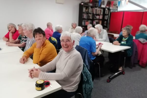 Cordite Club Quiz 2023 3 Three rows of tables with members of The Devil's Porridge Museum's Cordite Club sat at them. The person closet to the camera looks very happy.
