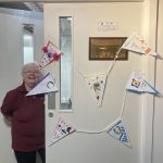 A member of our museum team, Wendy stood in the doorway of The Devil's Porridge Museum's education room which has bunting decorating it.