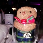 A toy bear wearing a bow tie and a kilt sitting in a wine glass.