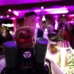 A toy bear stood on two wine bottles at South of Scotland Thistle Awards regional final. One of the museum's volunteer is blurred in the background.