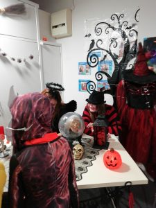 A child dressed as a Monster from Stranger Things stands in front of a table containing an assortment of Halloween paraphernalia including a plastic crystal ball. Two members of our museum team sit behind the table dressed as an angel and Freddy Krueger.