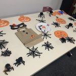 A table containing items that the young people at this workshop has made. This includes paper pumpkins, a few masks, one trick or treat bag, pipe cleaner spiders and spiders webs.