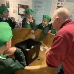 School children gathered around a nitrating pan on display in The Devil's Porridge Museum with one of the museum's volunteers.