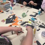 A young persons hands reaching out on a table covered with craft supplies.