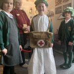 Three school children dressing up with one of The Devil's Porridge Museum's trustees in the background.
