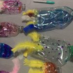 Some plastic bottles upcycled to make fish with feathers and felt tip pen drawings on them.
