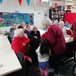 A child talking to some pensioners. The pensioners are sat down at rows of tables.
