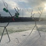 Two metal reindeers are stood outside in the snow. Some baubles hang from their antlers.