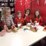 A group of six children gathered around table with festive items they made on it.
