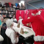 Santa gives out Christmas gift bags to a table of people.