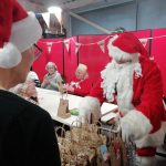 A trolly full of Christmas gift bags attended by Santa and one of the museum's trustees, who wears a Santa hat.