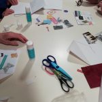 Some scissors, pens, glue and other craft materials on a table.