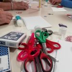 Some scissors, glue, card and scissors arranged on a table.