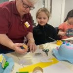 A museum volunteer helping a child to decorate an Easter bonnet.