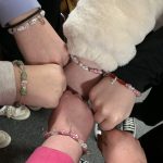 A circle of hands wearing bracelets.