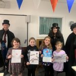 Spooky storytellers, Mostly Ghostly and the young people who came to the storytelling event at The Devil's Porridge Museum. The young people are holding artwork. They look happy.