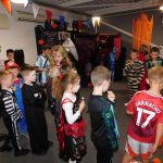 Young people in Halloween costumes lining up to play a Halloween game. This is happening in The Devil's Porridge Museum's education room, which is decorated for Halloween.