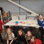 Happy young people from Arts and Crafts club gathered around a table with their handmade creations on.