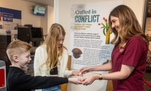 A member of The Devil's Porridge Museum's team giving some badges to two young people.