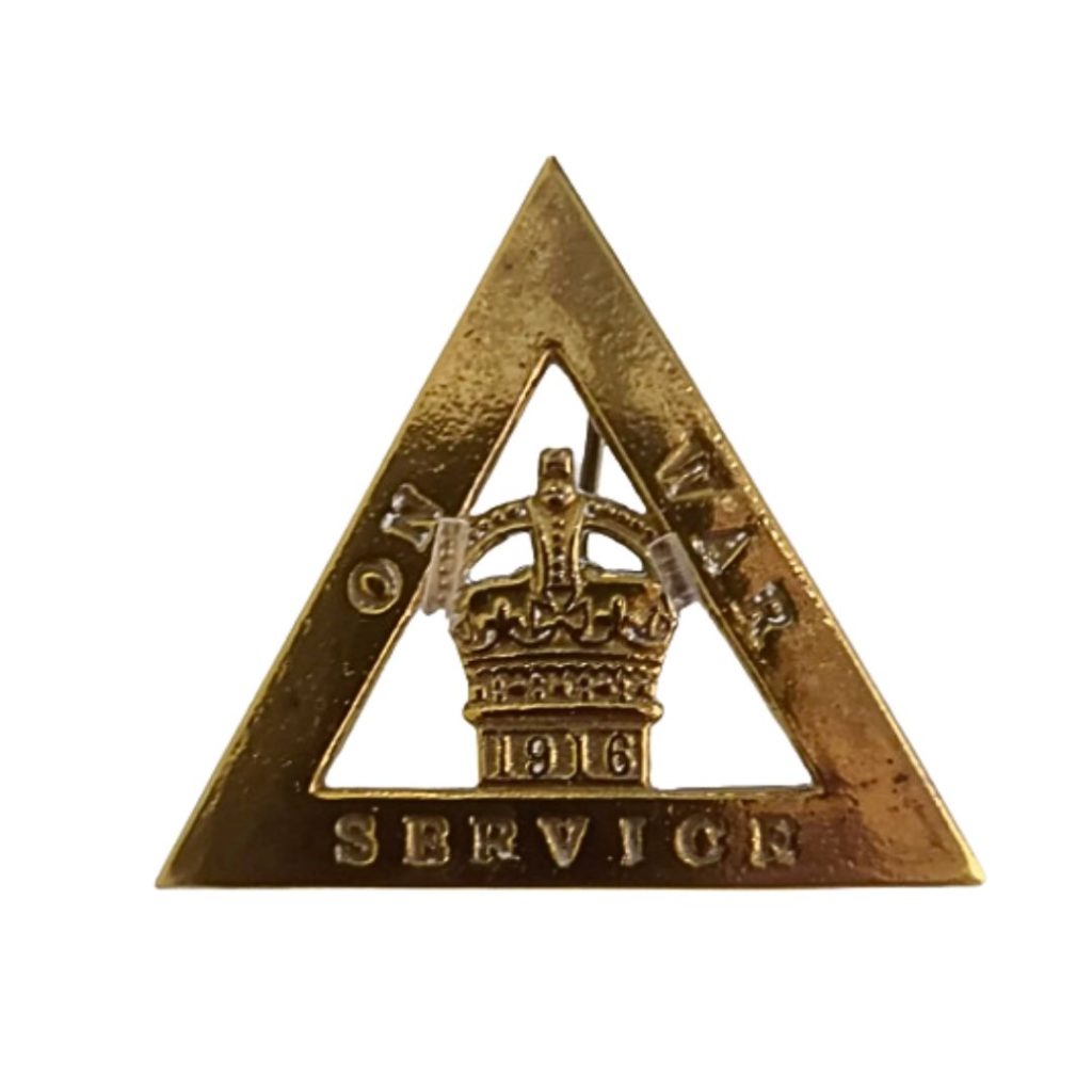 A triangle shaped, brass On War Service badge. There is a crown inside the triangle with 1916 underneath it.