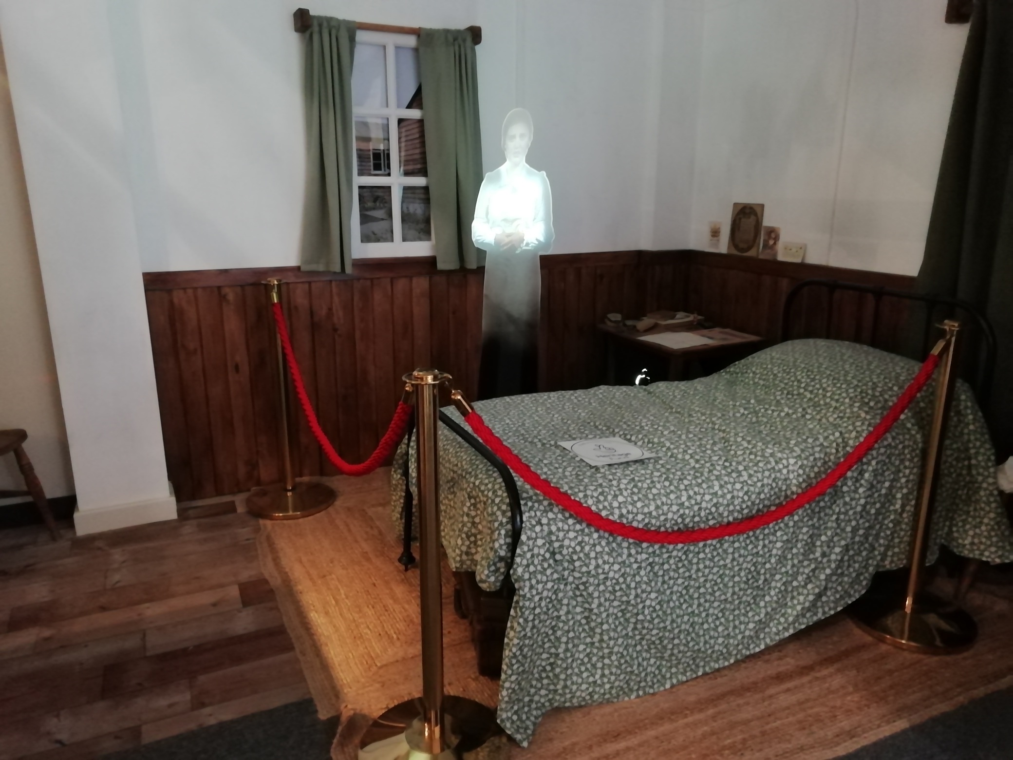 Munition workers dormitory display inside The Devil's Porridge Museum. There is a bed and a projection or hologram of a munition worker.